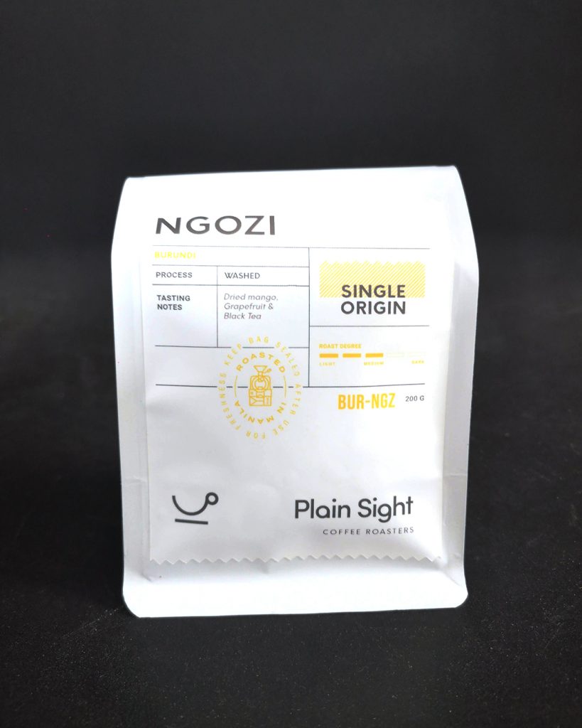 One bag of Plain Sight Coffee's Ngozi varietal, front-facing with a black backdrop. Silver tall packet with minimalist label accented with yellow elements.