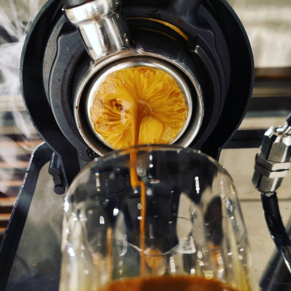 A photo taken of the underside of a portafilter as it pulls a shot of espresso.