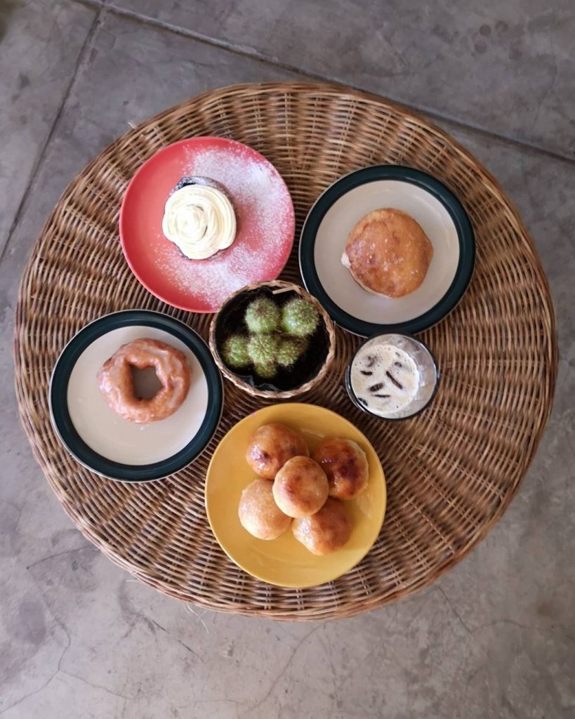 A top shot of a basket with a selection of Masa Bakery's pastries. On the center of the basket is a small cactus in a pot, surrounded by four plates of varying sizes and colors.  One each plate is a different kind of pastry. In between two of these plates is a glass filled with beverage.
